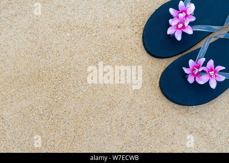 Bunte Flip-flops am Sandstrand. Hausschuhe, Schwarz mit rosa Blume auf dem Sand. Das Konzept der Sommer und Reisen. Stockfoto