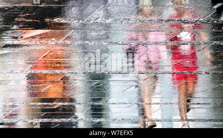 Unscharfe Reflexion Schatten Silhouetten, die laufen an einem regnerischen Fußgängerzone Stadt nasse Straße an einem Sommertag, in einer Pfütze Stockfoto