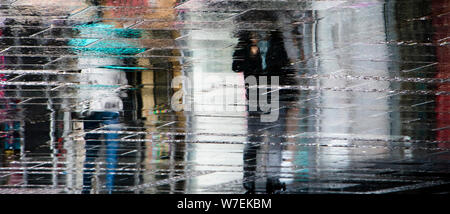 Unscharfe Reflexion Schatten Silhouetten, die laufen unter dem Dach an einem regnerischen Fußgängerzone Stadt nasse Straße, in einer Pfütze Stockfoto