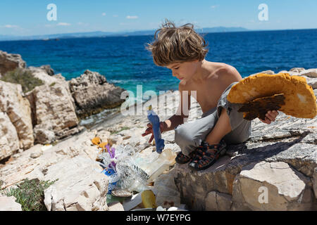 Little boy Reinigung Strand voller starrer Kunststoff Flaschen und anderer Müll raus an die Küste gespült. Stockfoto