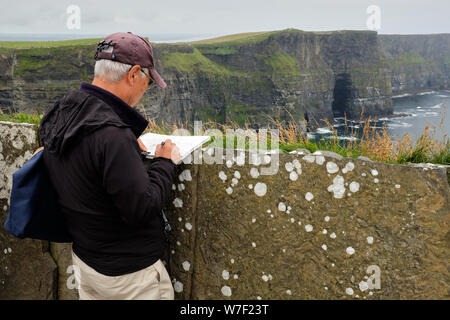 Touristische skizzieren die Landschaft an den Klippen von Moher auf einem grauen Regentag Stockfoto