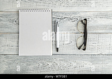 Notizbuch aus Papier, Stift und optische Gläser auf Vintage shabby weiß Holz- Hintergrund. Die Aussicht von oben. Flach Stockfoto