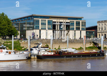 Die Banque Populaire Bretagne Centre Atlantique an Bastide-Niel, Bordeaux, Frankreich. Verschiedene Boote angedockt auf La Garonne Fluss vor dem Gebäude. Stockfoto