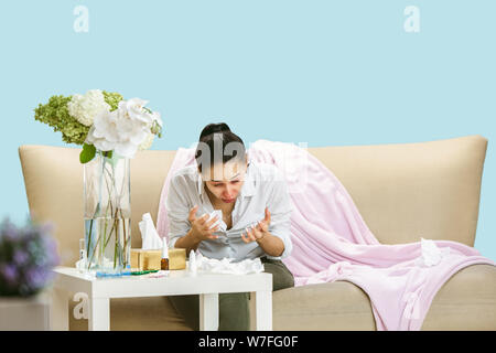 Junge Frau mit hausehold Staub oder saisonale Allergien. Niesen in der Serviette und sitzt von gebrauchten Servietten auf dem Boden und einem umgeben. Arzneimittel ohne Ergebnis. Healthcare Konzept. Stockfoto