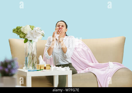 Junge Frau mit hausehold Staub oder saisonale Allergien. Niesen in der Serviette und sitzt von gebrauchten Servietten auf dem Boden und einem umgeben. Arzneimittel ohne Ergebnis. Healthcare Konzept. Stockfoto