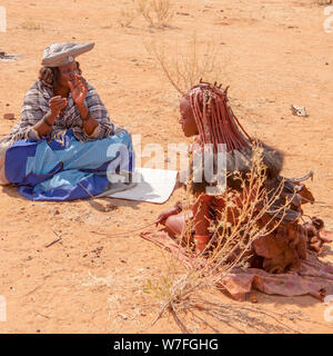 Herero, Himba Frauen an einem Begräbnis sammeln, Zelte und Hütten können im Hintergrund gesehen werden. Kaokoveld, Namibia Stockfoto