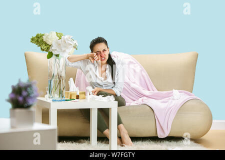 Junge Frau mit hausehold Staub oder saisonale Allergien. Niesen in der Serviette und sitzt von gebrauchten Servietten auf dem Boden und einem umgeben. Arzneimittel ohne Ergebnis. Healthcare Konzept. Stockfoto