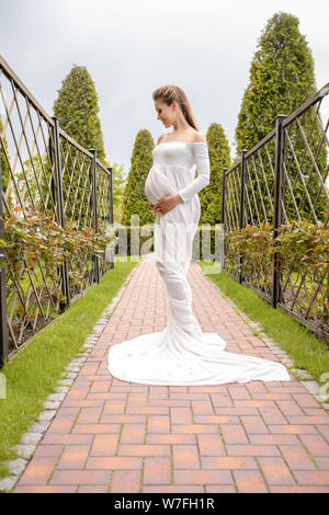 Eine schöne und einfache Schwangerschaft. Einen langen weißen Zug aus dem Bauch einer Schwangeren schönes Mädchen im Freien Stockfoto