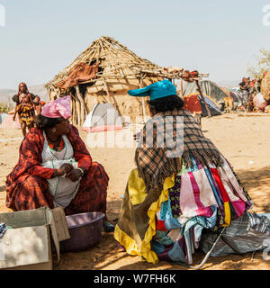 Herero Frauen an einem Begräbnis sammeln, Zelte und Hütten können im Hintergrund gesehen werden. Kaokoveld, Namibia Stockfoto