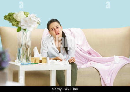 Junge Frau mit hausehold Staub oder saisonale Allergien. Niesen in der Serviette und sitzt von gebrauchten Servietten auf dem Boden und einem umgeben. Arzneimittel ohne Ergebnis. Healthcare Konzept. Stockfoto