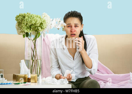 Junge Frau mit hausehold Staub oder saisonale Allergien. Niesen in der Serviette und sitzt von gebrauchten Servietten auf dem Boden und einem umgeben. Arzneimittel ohne Ergebnis. Healthcare Konzept. Stockfoto