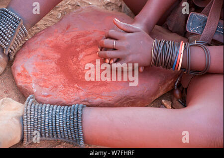 Frau Himba zerquetscht roter Tonerde, dieser wird dann verwendet, um Ihr Haar auftragen. In einem Himba Dorf fotografiert, Epupa Wasserfälle, Kaokoveld, Namibia, Afrika Stockfoto