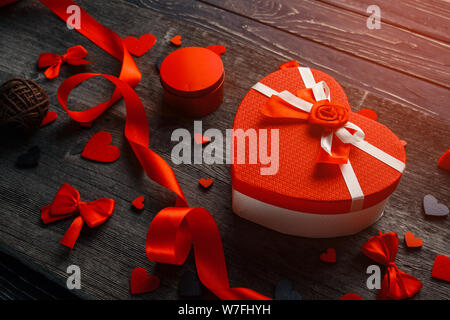 Herzförmige Geschenkbox mit Filzherzen und Satinband auf einem Holzhintergrund. Komposition mit Geschenk, geschenkbox, rote Herzen. Stockfoto