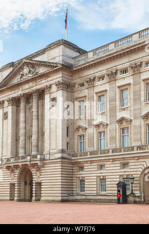 Ein Soldat in roter Uniform tragen eines traditionellen Busby, Mitglied des Queen's Guard, steht die Aufmerksamkeit auf die Wache am Buckingham Palace, London Stockfoto