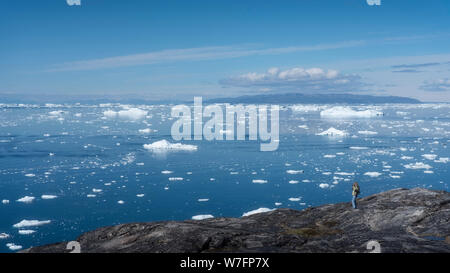 Ein Tourist an der Diskobucht mit Eisblöcke aus dem Ilulissat Eisfjord, in der Nähe von Ilulissat in westlichen Grönland. Stockfoto