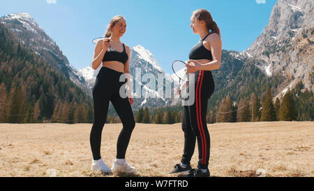 Zwei junge Frauen, die auf dem Feld und mit dem Sprechen, nachdem Badminton Spiel - Dolomiten, Italien Stockfoto