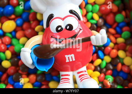 M&M's Red candy Dispenser von einem Koch mit Schüssel und Löffel auf einem Haufen von M&Ms bunten Süßigkeiten-beschichteten Pralinen Stockfoto