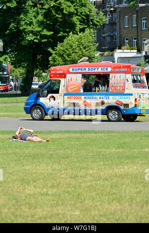 Junge Frau relaxen in der Sonne mit dem Mobiltelefon neben ein Eis und Hot Dog van, Clapham Common South West London, Vereinigtes Königreich Stockfoto