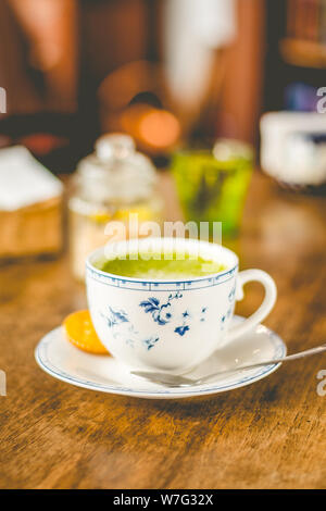 Grüner Tee matcha Soja Latte in einem China Schale mit braunem Zucker und ein Glas Wasser auf der Seite Stockfoto