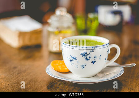 Grüner Tee matcha Soja Latte in einem China Schale mit braunem Zucker und ein Glas Wasser auf der Seite Stockfoto