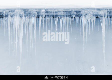 Eiszapfen hängen auf dem Dach über hellblau Wand Hintergrund Stockfoto
