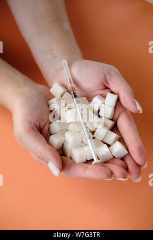 Frau mit weißen Würfel Zucker und Insulin Spritze auf orangem Hintergrund. Diabetes, Zucker Krankheit, ungesundes Essen, Diät Konzept. Platz kopieren Stockfoto