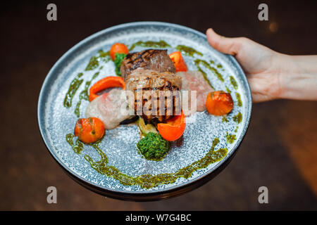 Mitte - gebratenes Fleisch mit Gemüse auf blauem Teller in einem Restaurant. Stockfoto