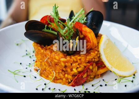 Spanische Paella mit Muscheln und Garnelen mit Zitrone und Rucola. Auf einem weißen Teller mit Zitrone serviert. Closeup fo einen schönen Reisgericht. Stockfoto