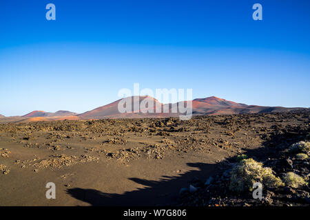 Spanien, Lanzarote, Roter Vulkan Berge von Timanfaya Nationalpark hinter endlosen schwarzen Lavafeld Stockfoto