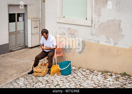 Nazare, Portugal - Juli 19, 2019: ein Restaurant Mitarbeiter außerhalb sitzt in den Straßen von Sitio Schälen von Kartoffeln Stockfoto