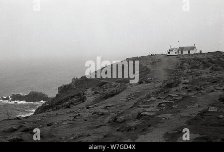 70er Jahre, Bild zeigt die zerklüftete Küste von Land's End, Cornwall, England, mit dem berühmten Teestube, dem "First & Last House" auf dem Festland Großbritanniens, auf der Klippe mit Blick auf den Ozean. Ursprünglich ein kleines einstöckiges Haus, das im 19. Jahrhundert für Gracie Thomas erbaut und als Souvenirladen geführt wurde, wurde es im Laufe der Jahre erweitert, bleibt aber ein wichtiges Wahrzeichen an dieser besonderen Lage. Stockfoto