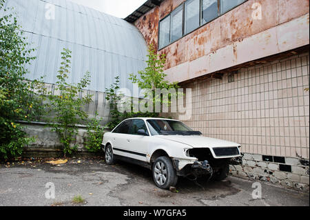 Weißes Auto ohne Licht, Stoßfänger und egine in der alten Fabrik demontiert. Stockfoto