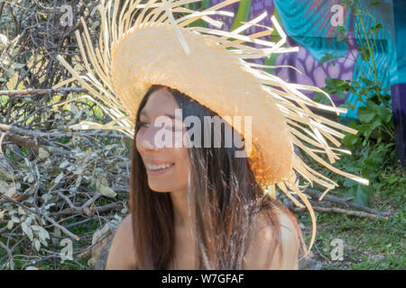 Jungen Südamerikanischen Frau mit einem Strohhut auf dem Kopf, um sich von der Sommersonne während eines Picknicks in der Natur zu schützen, Spaß und Smil Stockfoto
