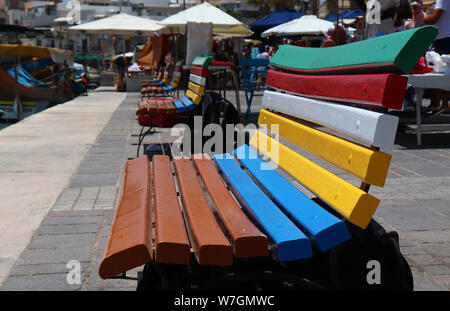 Bänke in traditionellen maltesischen Farben am Kai in Marsaxlokk, Malta malte Stockfoto