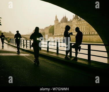 Unter der Brücke an der Seine an einem regnerischen Sommertag in Paris Frankreich. Ein Mädchen ihre Fotos auf Ihrer Kamera als drei Elektroroller vorbei. Stockfoto
