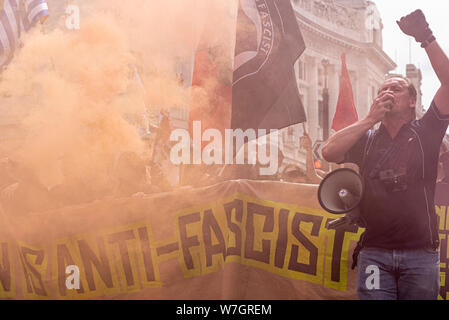 Antifa, antifaschistische Demonstranten in Opposition bei der Free Tommy Robinson Protestkundgebung in London, Großbritannien. Banner, Marktführer mit Megaphon. Farbiges Rauchfackeln Stockfoto