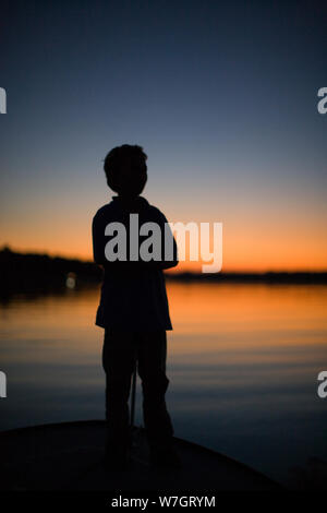 Silhouette Junge auf dem Boot bei Sonnenuntergang Stockfoto