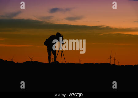 Ein Fotograf in Silhouette mit einer DSLR-Kamera und Stativ fotografieren bei Sonnenuntergang. Stockfoto