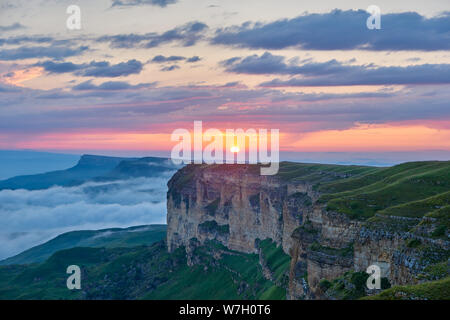 Sonnenuntergang in den Bergen. Die untergehende Sonne beleuchtet die Bergkette, Nebel und Wolken. Stockfoto