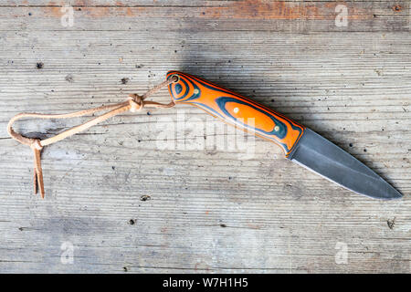 Blick von oben auf die handgefertigte geschwärztem Stahl Messer mit hausgemachten Epoxid- und orange Stoff Griff mit Lederband auf alten Holz- Board Stockfoto