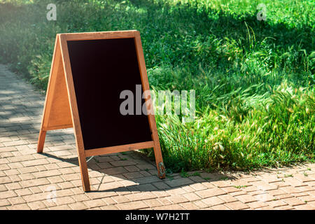 Eine Schwarze Schiefertafel stehen auf Holz für ein Menü im Restaurant auf der Straße. Leeres Menü auf Straße. Leeres Menü auf Straße auf der Pub oder Restaurant Stockfoto