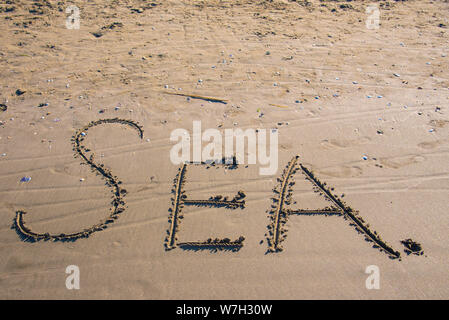 Das Wort "EA" in das dunkle Meer Sand an einem sonnigen Tag geschrieben, Konzept Symbol für Urlaub Stockfoto