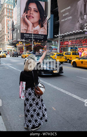 Eine Frau steht auf der Straße ein Taxi Hagel auf einer belebten Straße in Times Square, Midtown, New York Stockfoto