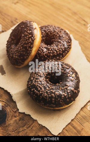 Drei süße Krapfen mit Schokolade und Sahne Krümel auf rustikalen Holztisch Stockfoto