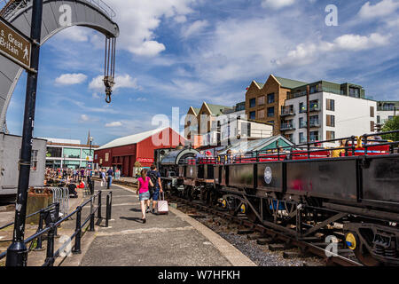 Menschen zu Fuß zwischen Hafen und Eisenbahn Dampf Kran am Kai des Prince's Wharf, Bristol, UK. Juli 2019. Stockfoto