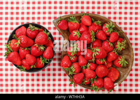 Von oben nach unten anzeigen, Erdbeeren in Schwarz und aus Holz geschnitzte Schale auf Red gingham Muster Tischdecke Stockfoto