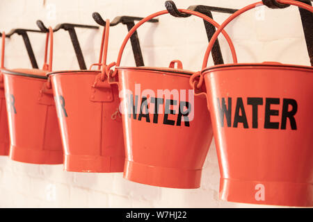 Rote Eimer mit dem Wort Wasser auf der Seite für die Brandbekämpfung Stockfoto