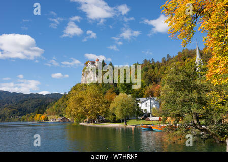 Bäume in Herbstfarben am Ufer des Bleder Sees und die Burg von Bled auf einer Klippe hoch über dem See an einem schönen Herbsttag in Bled, Slowenien. Stockfoto