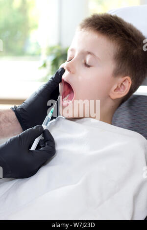 Die Hände der Zahnarzt in schwarzem Latex Handschuhe halten Anästhesie. Der junge mit geschlossenen Augen und Mund weit geöffnet sitzt auf dem Behandlungsstuhl. Stockfoto