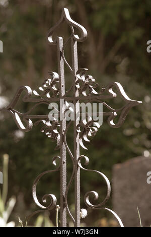 Alte schmiedeeiserne Kreuz neben dem Grab. Grüner Hintergrund mit unscharfen Laub. Selektiver Fokus auf das Kreuz. Stockfoto